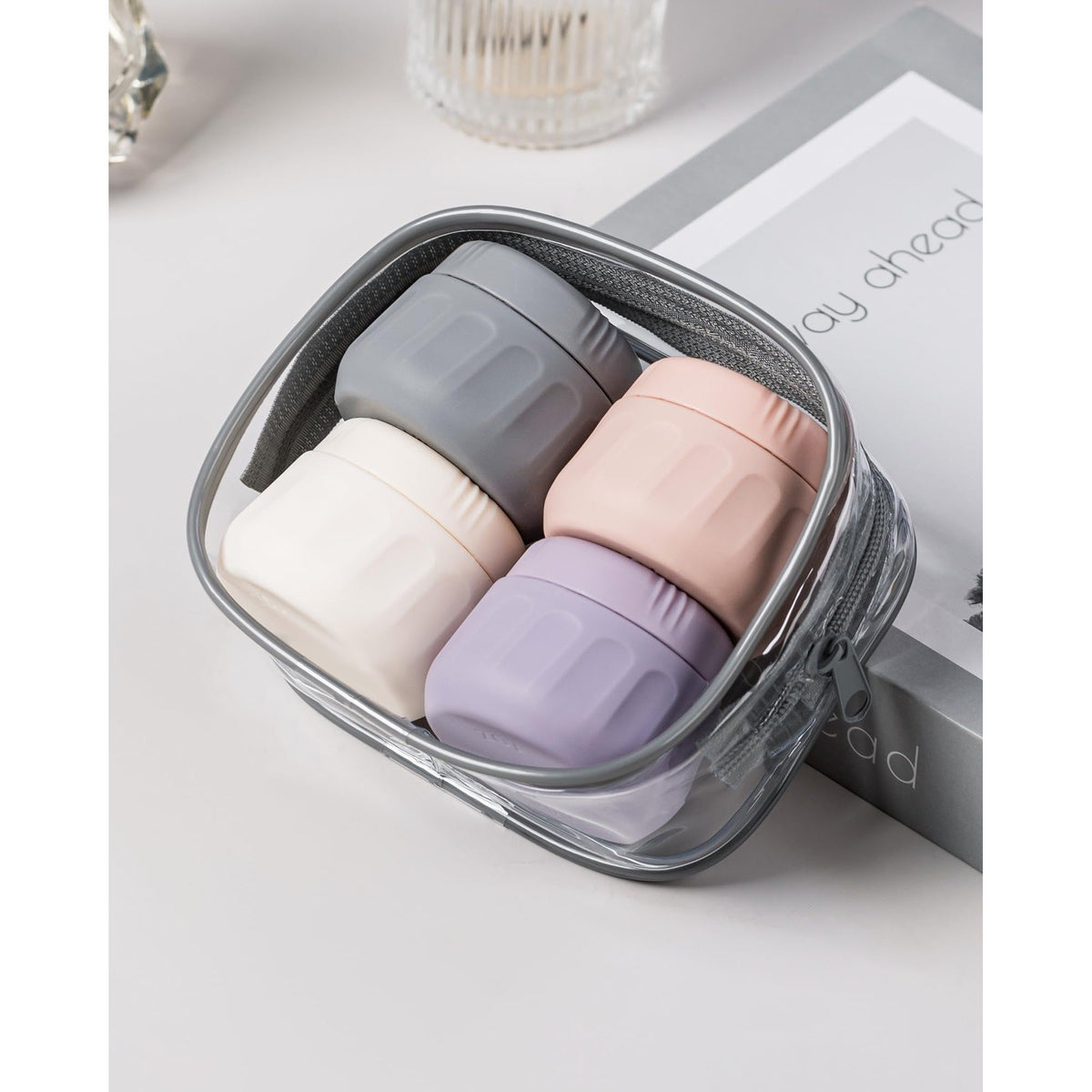 Four silicone travel containers in gray, pink, white, and lavender, neatly packed in a clear zippered pouch.