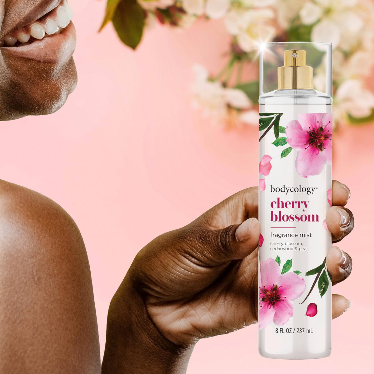 A woman smiles while holding Bodycology Cherry Blossom Fragrance Mist. Enjoy a floral scent with notes of cherry blossom and cedarwood. Verified by CuratCart.