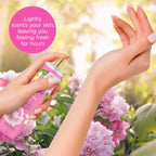 A hand spritzes Bodycology Long-Lasting Fragrance Body Mist surrounded by blooming peonies, perfect for lasting freshness.