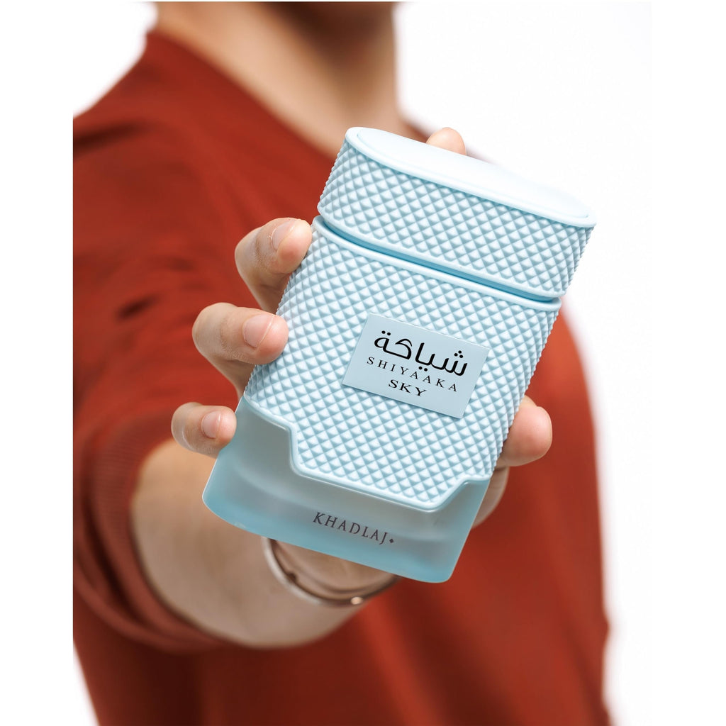 A person holds a stylish Khadlaj Shiyaaka Snow perfume bottle, featuring a unique textured design and a refreshing citrusy, woody scent.