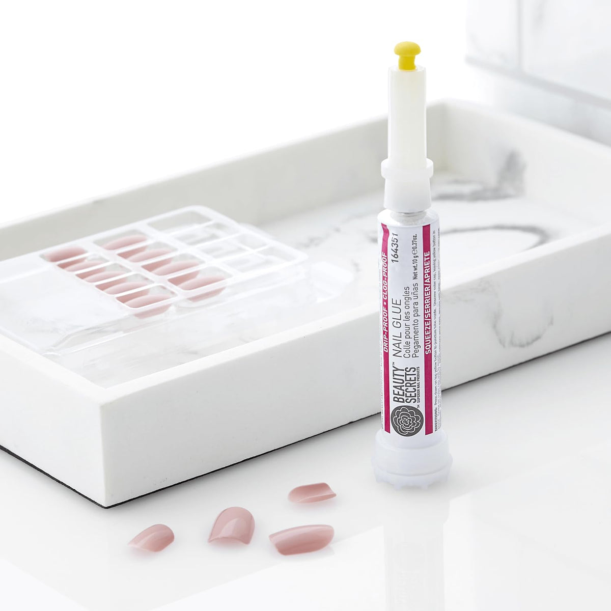 Beauty Secrets drip & clog proof nail glue in a tube, with false nails displayed on a marble tray.
