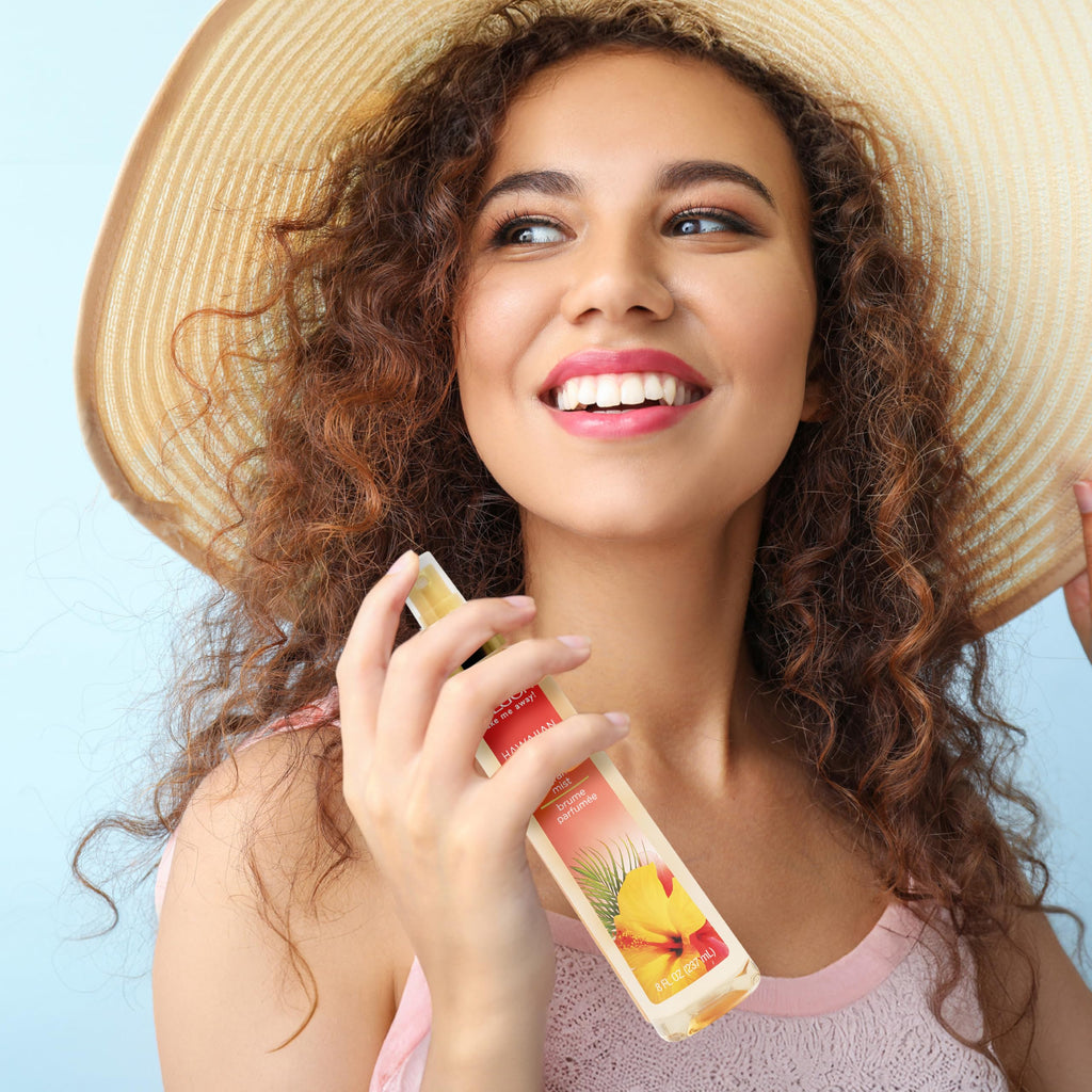 A smiling woman with curly hair holds Calgon Fragrance Body Mist, Morning Glory, showcasing its vibrant packaging and refreshing scent.