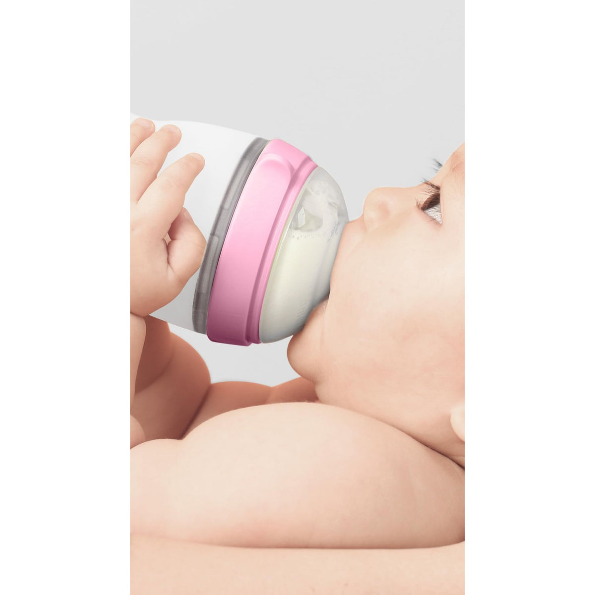 A baby comfortably sipping from a pink Comotomo baby bottle. Verified by CuratCart for quality assurance.