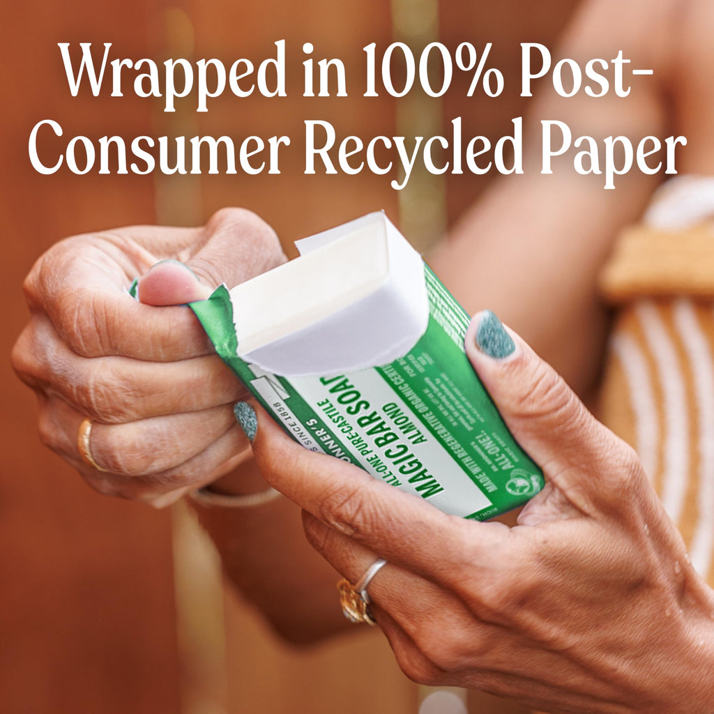 A person holds Dr. Bronner's Pure-Castile Bar Soap, wrapped in 100% post-consumer recycled paper, showcasing its eco-friendly packaging.