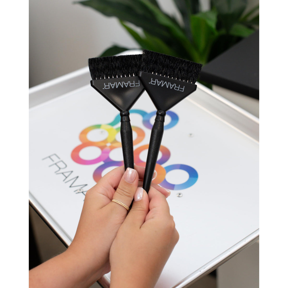 Two Framar hair color brushes held by hands, showcasing quality design. Verified by CuratCart for trusted shopping.
