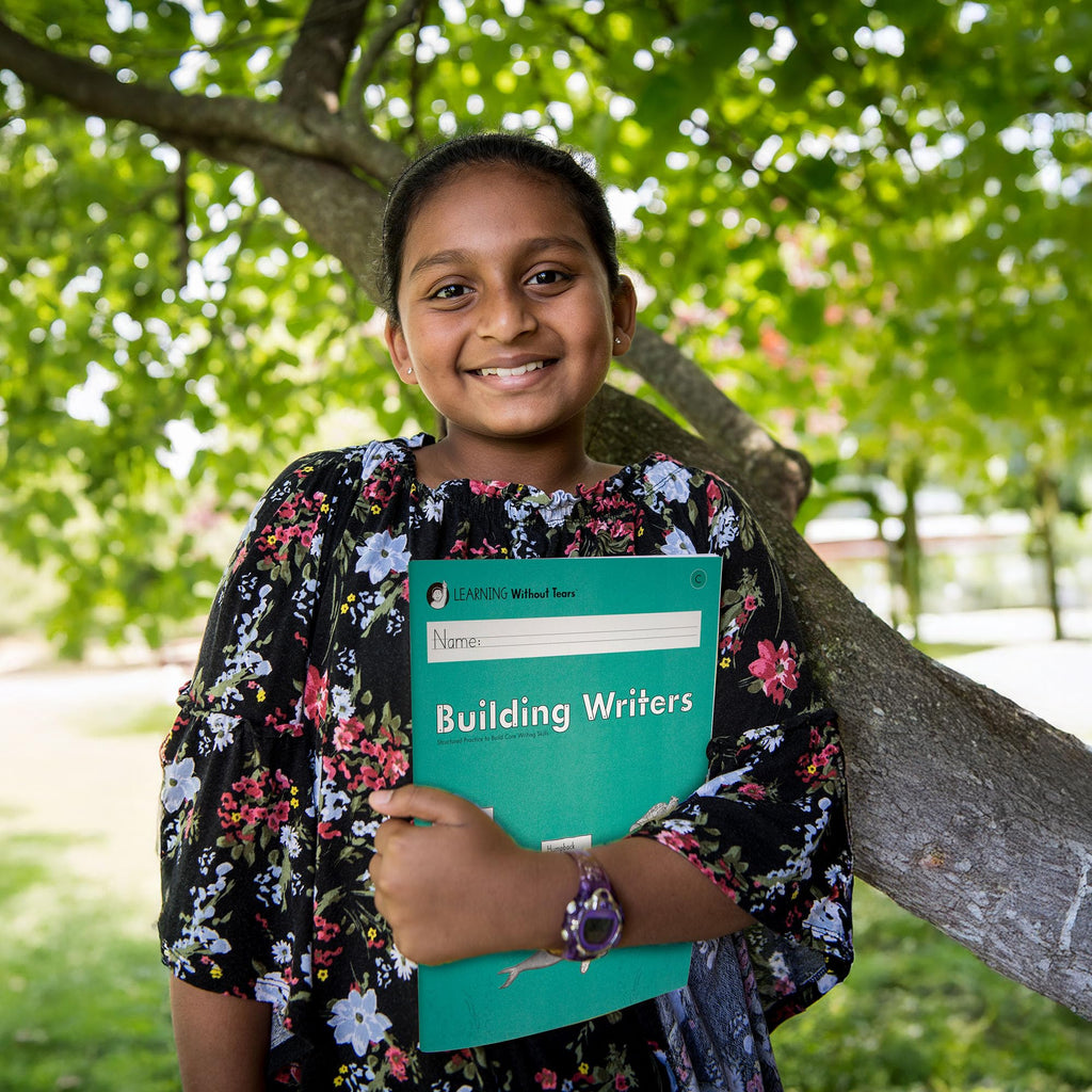 A smiling girl holding the Learning Without Tears Building Writers workbook outdoors, showcasing trust and availability at Curat Cart.