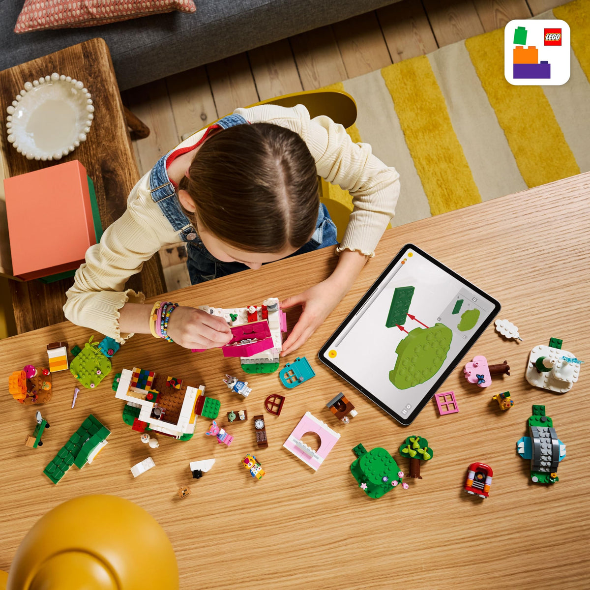 A child constructs the LEGO Animal Crossing Creative Houses set amid colorful bricks and an iPad, showcasing creativity and fun.