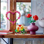 Brightly colored LEGO heart ornament set with flowers on a shelf, alongside roses and a decorative vase. Verified by CuratCart.