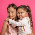 Two girls with playful smiles showcase Lip Smacker Sparkle & Shine Eyeshadow against a vibrant pink backdrop.