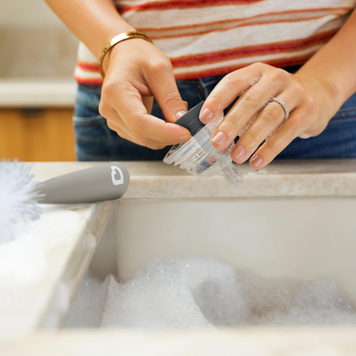 A person cleans a bottle with the Munchkin Sponge Bottle Brush in a soapy sink, showcasing its effective design.