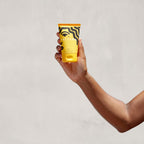 A hand holds a tube of PATTERN Beauty Curl cream in bright yellow packaging featuring bold, graphic design.