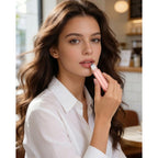 A woman applies essential oils using a pink roller bottle, showcasing the product in a stylish cafe.