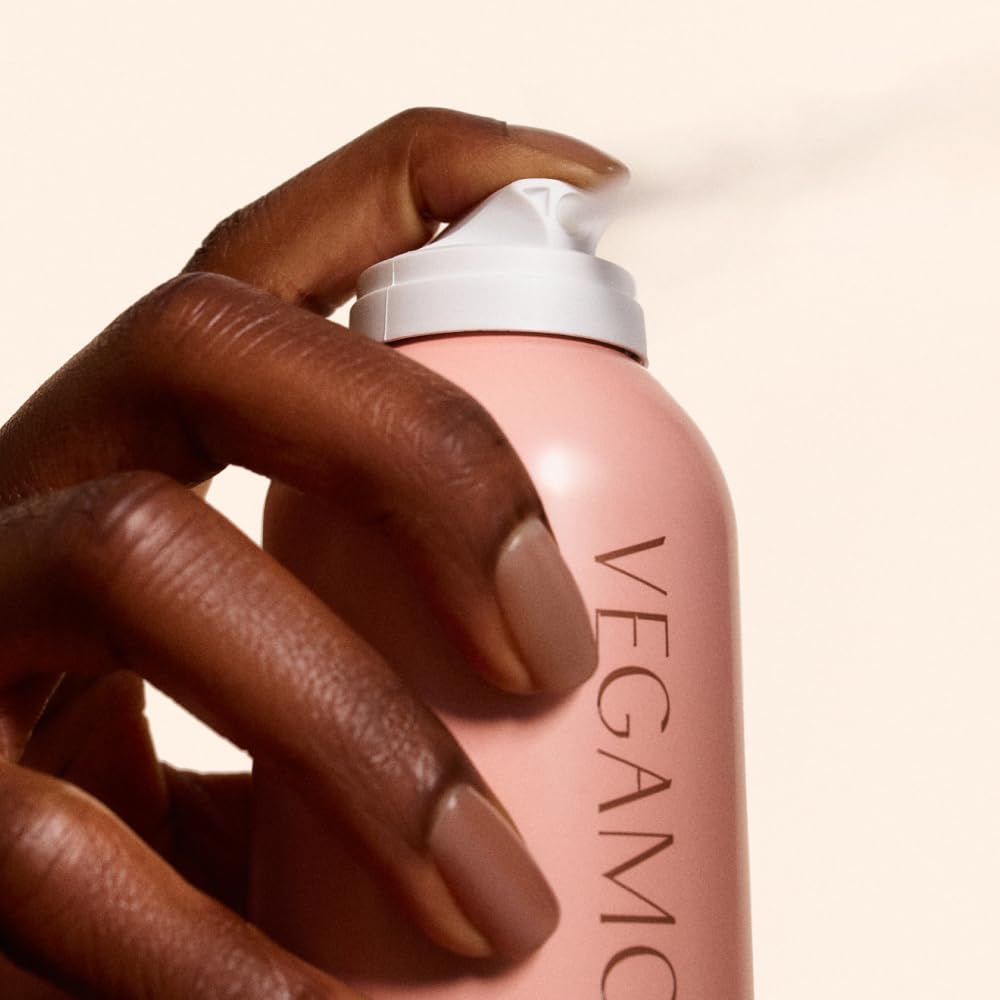 A hand holding VEGAMOUR GRO Dry Shampoo bottle, showcasing its sleek design. Trusted by CuratCart for quality.